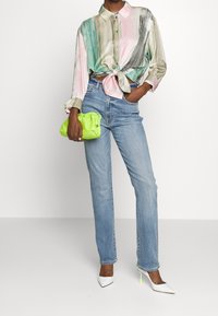 Silkkipaita, jossa on vihreitä, vaaleanpunaisia ja kultaisia raitoja, solmittu vyötärölle; vaaleansiniset suorat farkut; kirkas vihreä käsilaukku; valkoiset korkokengät.