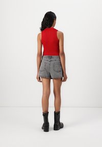 Haut sans manches rouge à côtes, short en denim noir et bottes noires à cheville. Le short a un ourlet effiloché et deux poches arrière.