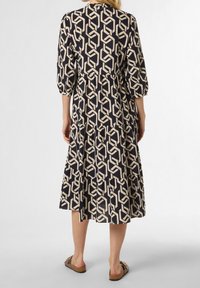 Navy mekko, jossa on vaaleanbeige geometrian kuvio, kolmanneksen pituiset hihat, kerroksellinen muotoilu, pehmeä kangas ja rento malli, yhdistettynä tasapohjaisiin sandaaleihin.