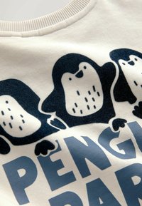Crème-kleurige sweatshirt met een marineblauwe pinguïn grafiek met stippenpatronen en grote blauwe tekst met de tekst "PENGUIN PALS." Zachte stoftextuur.