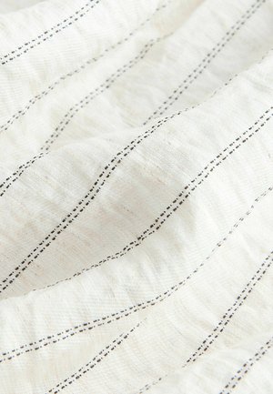 Közeli kép puha fehér anyagról, egyenletesen elhelyezett vékony fekete függőleges varrásokkal és texturált felülettel.