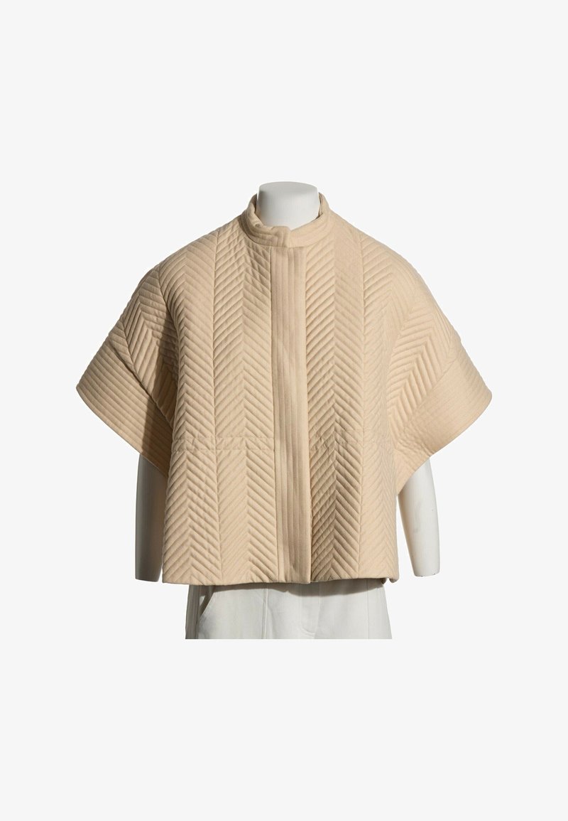Veste beige matelassée à manches courtes avec surpiqûres en chevron et col montant sur un mannequin blanc.