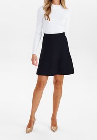 Falda negra en línea A con una textura suave, combinada con una camisa blanca ajustada de manga larga. El calzado consiste en tacones puntiagudos color nude.