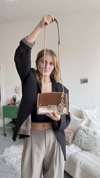 Brun og kremfarget strukturert håndveske med kjedestropp, krokodillemønster, gullfarget beslag og en dekorativ tag med slangeskinnsmønster.