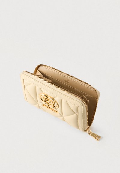 Portefeuille matelassé beige en matériau synthétique, doté d'un accent logo doré, d'une fermeture éclair et de compartiments internes pour cartes et espèces.