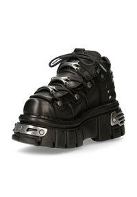 Stivale platform in pelle nera con suola spessa e scolpita, dettagli metallici e lacci neri infilati attraverso occhielli metallici a forma di fiamma.