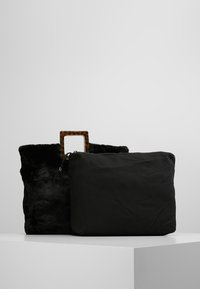 Svart päls handväska med ett sköldpaddsformat handtag och en avtagbar svart tygpåt. Har mjuk textur och rektangulär form.