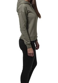 Olijfgroene hoodie met een voorzak, verstelbare trekkoordcapuchon, ribgebreide manchetten en onderrand, gedragen met zwarte skinny jeans.