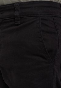 Črne denim hlače z gladko teksturo, ki imajo sprednji žep in zanke za pas. Tkanina ima minimalno vidne šive in enotno barvo.