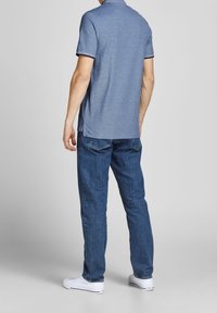 Blue polo shirt with a collar, short sleeves, and black trim. Paired with blue jeans and white sneakers. Smooth texture, casual fit.