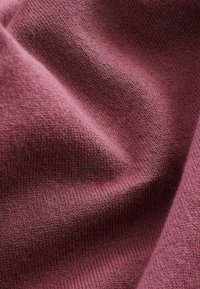 Struktureret stof i en dyb mauve farve med en glat overflade, der har fine strikmønstre og lette nuanceringer.