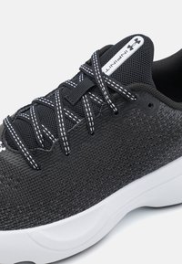 Zapatilla deportiva negra con parte superior de malla, media suela blanca y cordones negros en contraste. Presenta costuras blancas y una etiqueta de marca en la lengüeta.