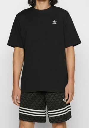 Schwarzes Baumwoll-T-Shirt mit kurzen Ärmeln, das ein kleines weißes adidas-Logo auf der Brust trägt. Getragen mit schwarzen Shorts mit weißen Streifen.
