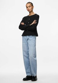 Czarny sweter z dzianiny z okrągłym dekoltem i zapięciem na guziki, w komplecie z jasnoniebieskimi luźnymi dżinsami i czarnymi sznurowanymi butami.