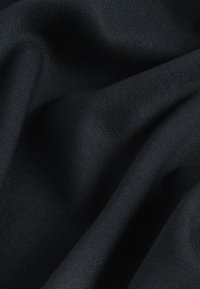 Zwarte textiel met een glad, licht gestructureerd oppervlak, met diepe plooien en kreukels die duiden op een flexibel materiaal.