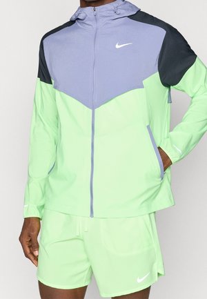Mann trägt neongrüne und hellviolette Nike Kapuzenjacke mit schwarzen Schulterpartien und passenden neongrünen Shorts.
