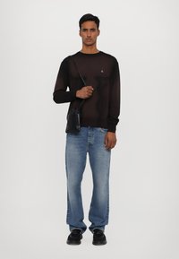 Svart, semi-transparent langermet genser med et lite brodert design; sammen med lyseblå, løstsittende jeans og svarte sko.