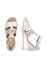 Wedge sandals with a beige faux leather upper featuring cut-out patterns, adjustable ankle strap, and a white ridged sole.