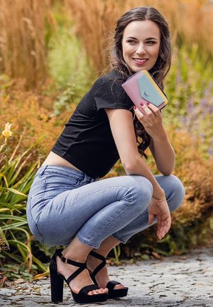 Light pink and blue wallet with a angled design held in a hand, paired with a black crop top, blue jeans, and black heeled sandals.