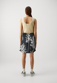 Strikket tanktop i beige med bølgete kanter, kombinert med et svart skjørt med hvite blomstermotiver, og grå sneakers.