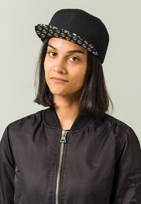 Must must, mille äärega, millel on mustriline aluspind. Mudel kannab musta bomber-jakki, millel on ees lukk ja soonikkoes kaelus.