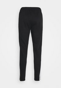 Pantalons de survêtement noirs en tissu doux, avec une coupe slim, des bandes latérales blanches et une taille élastique. Vue arrière affichée.