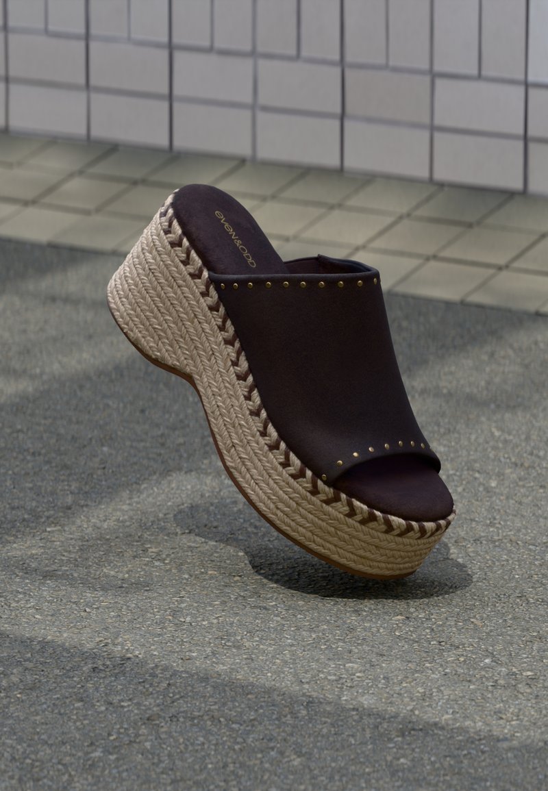 Μαύρο πλατφόρμα σανδάλι τύπου slip-on με πλεκτή σόλα από σκοινί και μεταλλικές λεπτομέρειες με τρουκς, σε υπόβαθρο πλακιδίων.