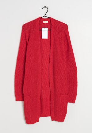 Długi czerwony sweter na drutach z odkrytym przodem, z dwoma przednimi kieszeniami, wiszący na czarnym wieszaku na białym tle.