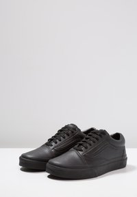 Sneaker in pelle nera con profilo basso, punta arrotondata, superficie testurizzata e lacci piatti. Presenta una suola in gomma e un design minimalista.