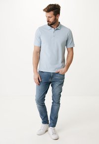 Světle modré polo tričko s krátkým rukávem a klasickým límcem se třemi knoflíky, v kombinaci s modrými džíny a bílými teniskami. Hladká textilie.