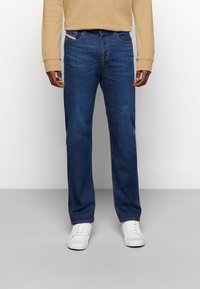 Mörkblå jeans med rak passform, tillverkade av denim, med en framficka och bälteshällor. Matchas med vita sneakers och en beige sweatshirt.