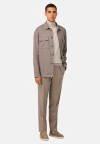 Ljusgrå knappad jacka med två framfickor, i kombination med en ljus tröja och matchande beige byxor samt slip-on skor.