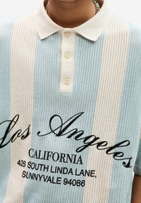 Světle modré a smetanově pruhované pletené polotričko s límečkem, zdobené vyšitým černým nápisem „Los Angeles“ a adresními detaily.