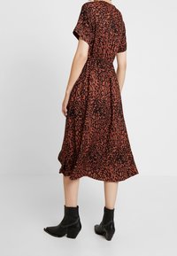 Braunes, mittelanger Kleid mit schwarzem Leopardenmuster, kurzen Ärmeln, elastischem Bund und einem ausgestellten Rock, kombiniert mit schwarzen Ankle Boots.