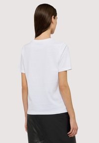 Camiseta de algodón blanca con mangas cortas, cuello redondo y un corte relajado. Textura simple y suave sin patrones ni gráficos visibles.