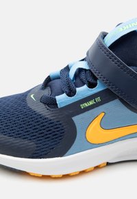 Tmavomodrá a svetlomodrá teniska Nike so žltým znakem, štítkom "Dynamic Fit", sieťovinovým zvrškom, šnúrkami a nastaviteľným pásikom na bielej podrážke.