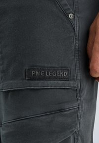 Tmavohnedé nohavice vyrobené z texturovanej tkaniny s označením PME Legend. Obsahujú ďalšie švy a kovový gombík ako detail.