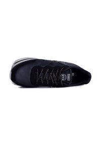 Schwarzer Sportschuh mit einem strukturierten Lederoberteil, runder Zehenpartie und weißer Sohle. Mit schwarzen Schnürsenkeln und einem runden Logo auf der Zunge.