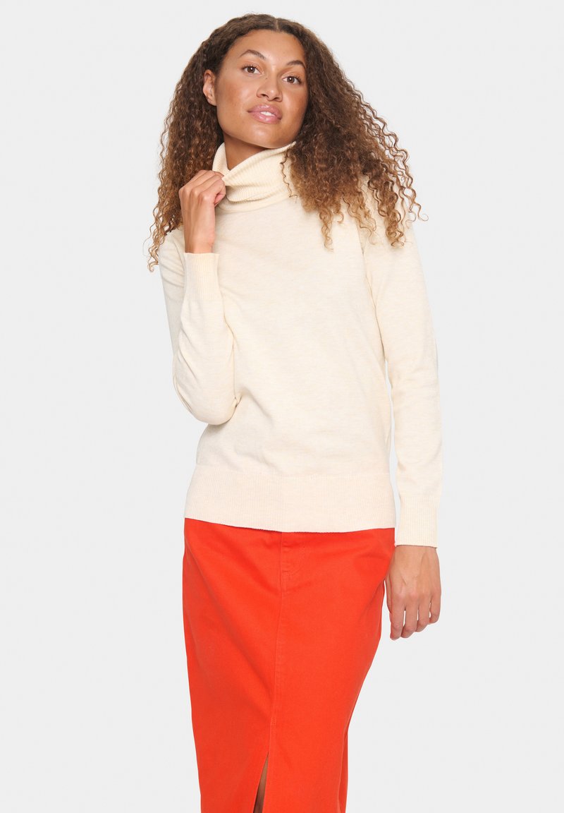 Cream turtleneck sweater with long sleeves, soft texture; paired with an orange skirt featuring a side slit. Neutral background.