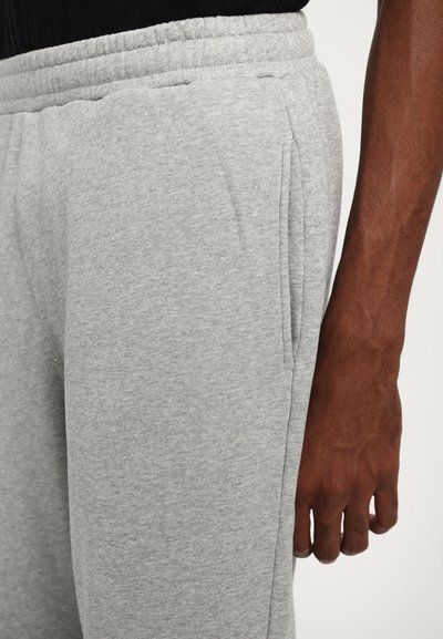 Light gray cotton sweatpants with an elastic waistband, side pockets, and a soft texture, shown next to a hand with a dark skin tone.