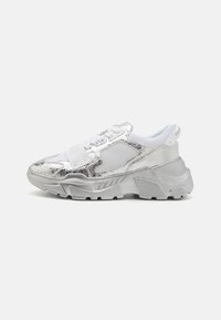 Sneaker argentato con una parte superiore metallica lucida, accenti in rete, lacci bianchi e una suola chunky. Finitura texturizzata con un design stampato.