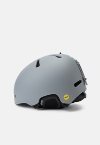 Pelēks slēpošanas ķivere ar MIPS tehnoloģiju, kurai ir ventilācijas atveres, gluda matēta apdare un regulējami siksnas, lai nodrošinātu drošu piegulšanu.