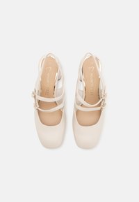 Chaussures slingback beiges avec un embout carré, dotées de double brides et d'accents de boucle. Matière en cuir lisse avec une semelle intérieure rembourrée.
