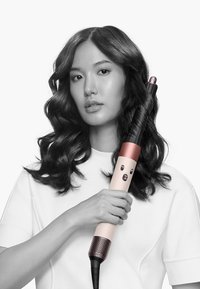 Locktång med svart texturerat handtag, roséguld och krämfärgad kropp samt rundad spets. Lång och smal form för styling av medellångt till långt hår.