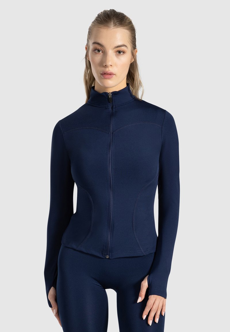 Marinblå zip-jacka i stretchigt material med långa ärmar och en figurnära design. Har sömdetaljer och hög krage.