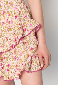 Saia com padrão floral em tons de rosa claro, verde e dourado. Camadas franzidas com detalhes em renda rosa. Cintura elástica para um melhor ajuste.