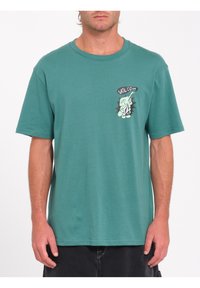 Camiseta de algodón color teal con mangas cortas, cuello redondo y un diseño gráfico que incluye la palabra "VOLCOM" y un personaje en el lado izquierdo del pecho.