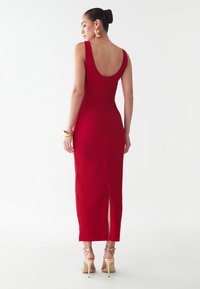 Punane, käeaukudeta kleit madala seljaga, külje lõhiku ja kehaülikonna kujuga. Sile materjal; ühendatud paljaste kontsade ja kuldsete ehtedega.