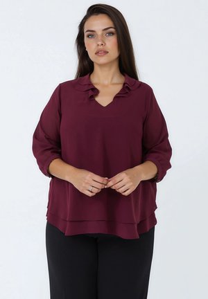 Bordeauxblouse met een V-hals en gerimpelde kraag, met lange mouwen en een gelaagd ontwerp. De stof lijkt lichtgewicht en soepel.