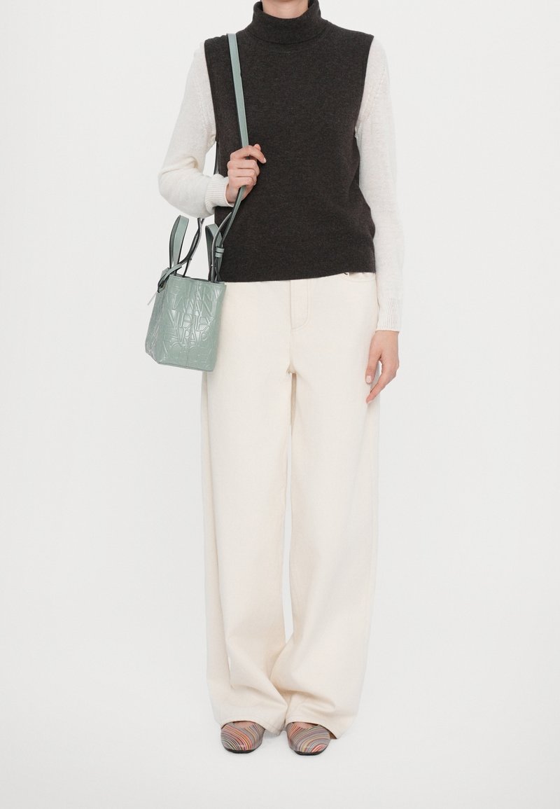 Tummanvärinen neule sleeveless-poolo, valkoinen pitkähiha, kermaiset leveälahkeiset housut, vihreä teksturoitu käsilaukku ja moniväriset kuvioidut liukumäkipohjaiset sandaalit.